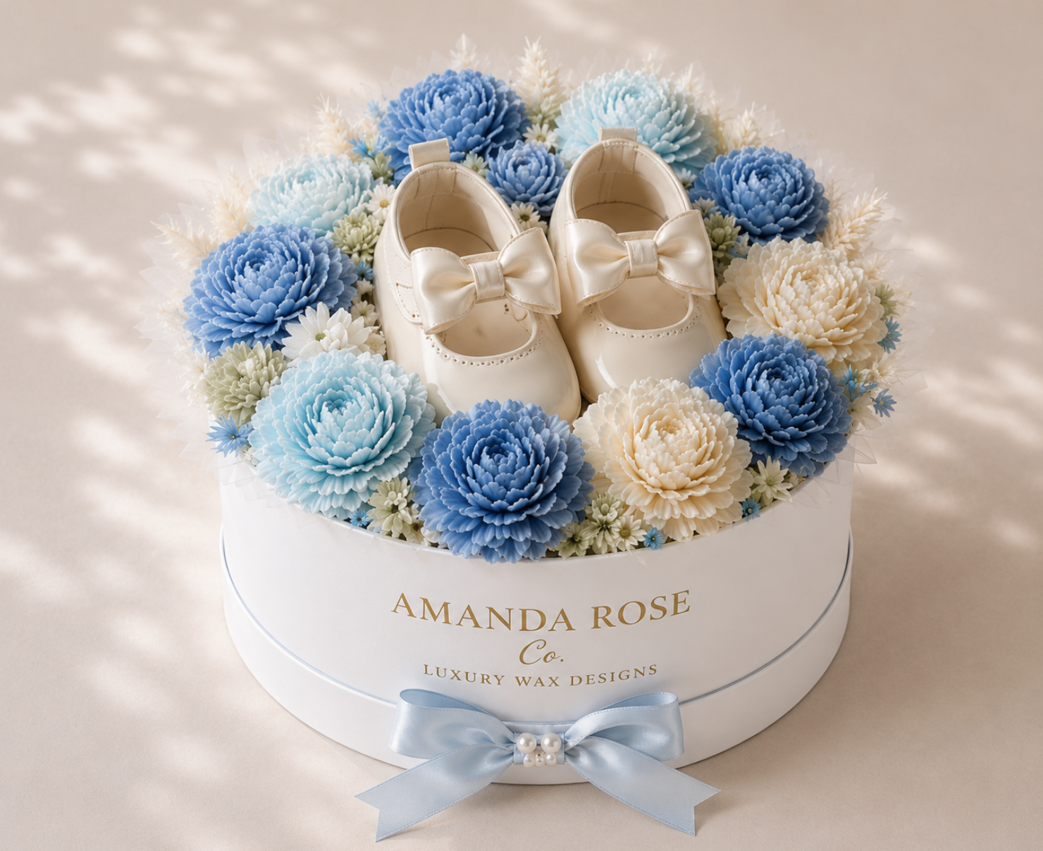 White baby shoes with bows surrounded by blue and white flowers in a 'Amanda Rose' box.
