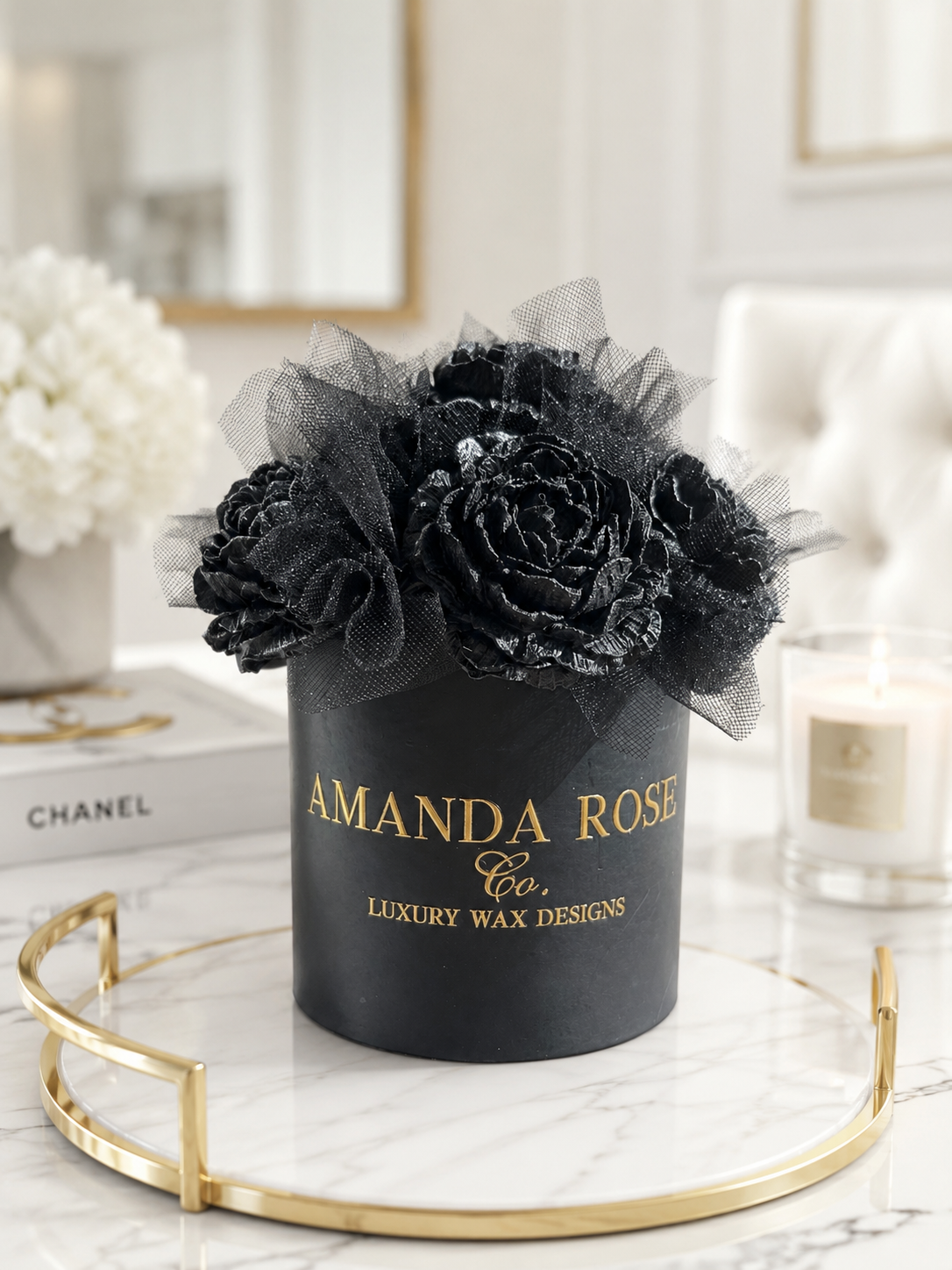 Black flower arrangement in a container with 'Amanda Rose Co.' branding on a marble surface.