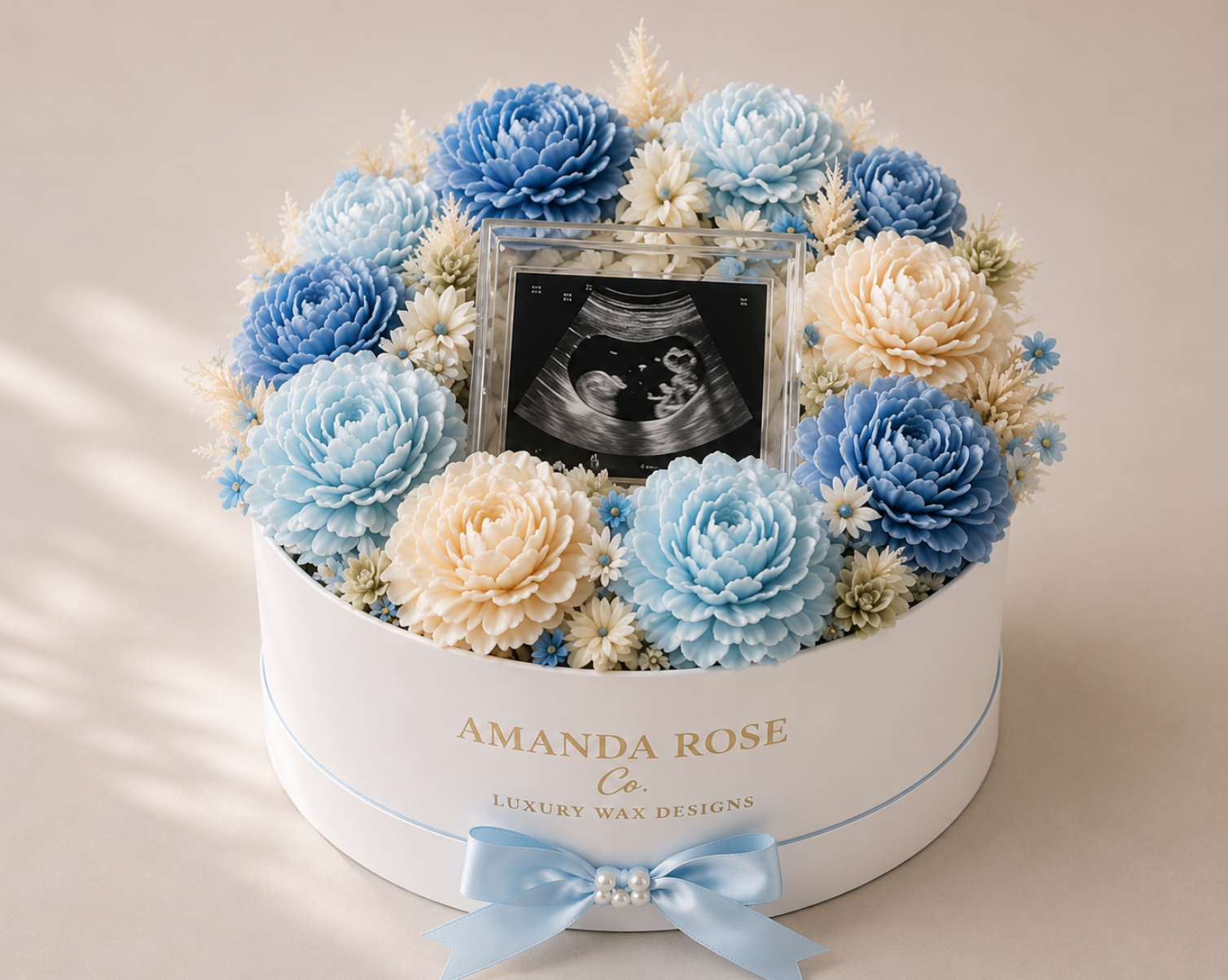 Floral arrangement with blue and beige flowers and an baby photo in a white box labeled 'Amanda Rose Co'.