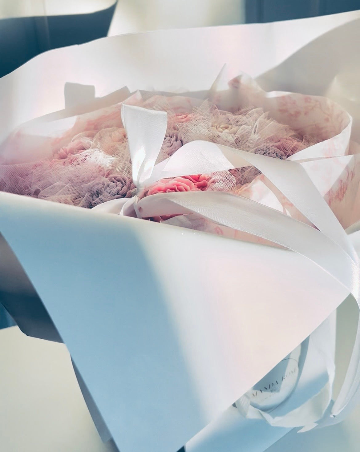 The Isabella bouquet of flowers wrapped in white paper with a ribbon on a light blue surface